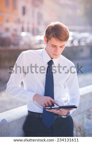 young handsome elegant blonde model man using tablet technological device in the city