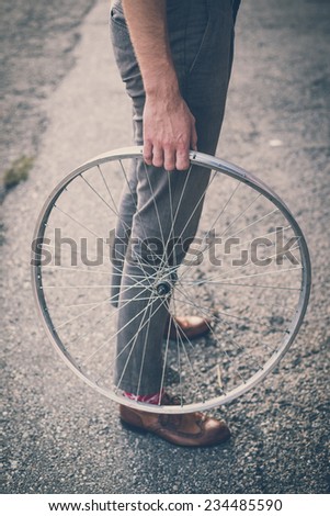 close up of legs shoes hipster man holding old bicycle wheel in the city