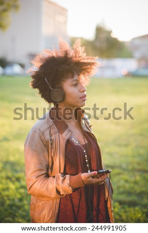 beautiful black curly hair african woman listening music with headphones in town