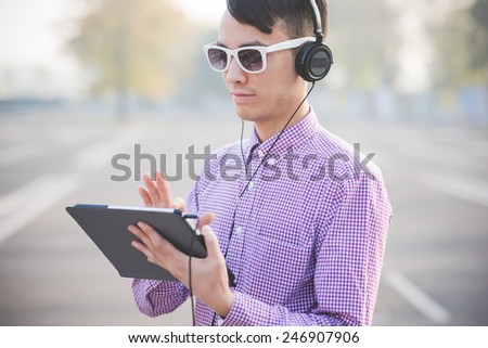 young crazy funny asian man in town outdoor lifestyle listening music with headphones and tablet