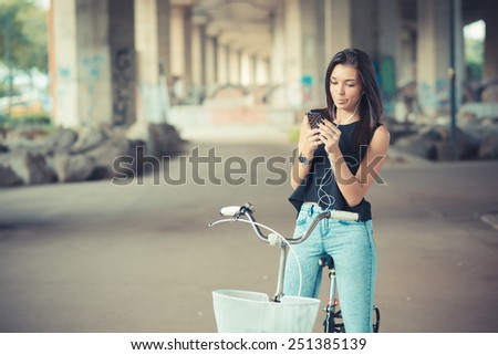 young beautiful brunette straight hair woman using bike and smartphone listening music outdoor