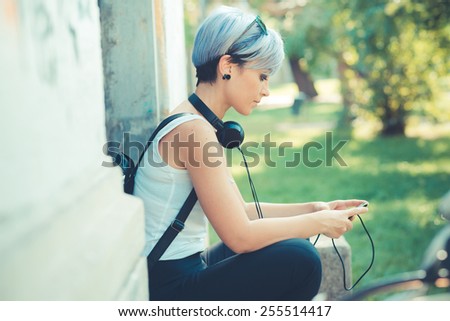 young beautiful short blue hair hipster woman with headphones music and bike in the city