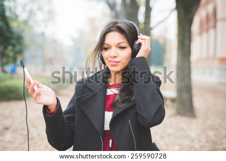 young beautiful indian woman at the park in autumn listening music with headphones