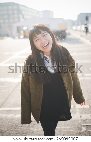 young beautiful asian hipster woman in the city - living town during sunset in backlit smiling happy having fun
