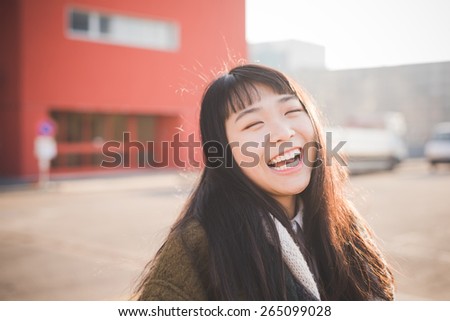 young beautiful asian hipster woman in the city - living town during sunset in backlit smiling happy