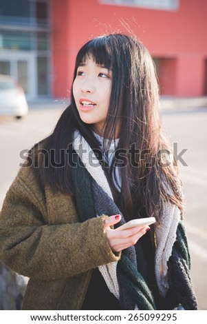 young beautiful asian hipster woman in the city - living town during sunset in backlit - using smartphone connected online