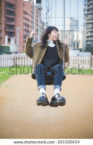 young beautiful asian hipster woman in the city - playing on a swing