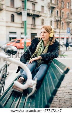 young beautiful hipster sporty blonde woman in town with bike and headphones