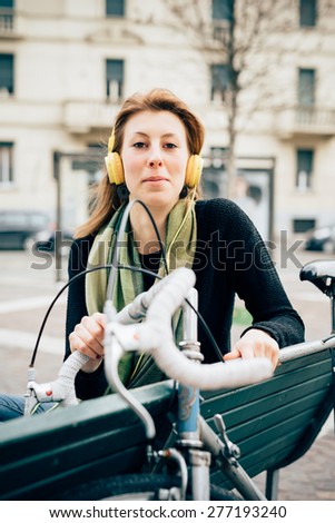 young beautiful hipster sporty blonde woman in town with bike and headphones