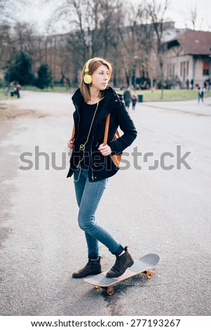 young beautiful hipster sporty blonde woman in town with skate bike and headphones