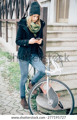 young beautiful hipster sporty blonde woman in town with skate and bike using smartphone