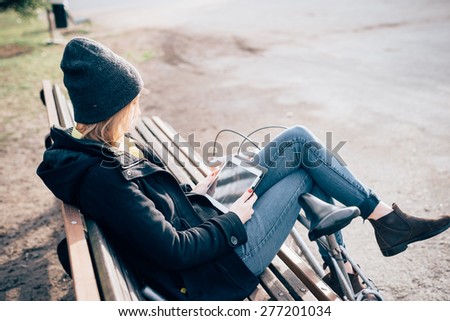 young beautiful hipster sporty blonde woman in town with bike using smartphone sitting in a bench