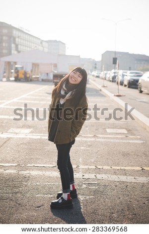 young beautiful asian hipster woman in the city - living town during sunset in backlit - smiling happy