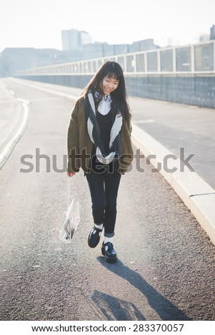 young beautiful asian hipster woman in the city - living town during sunset in backlit walking on the road