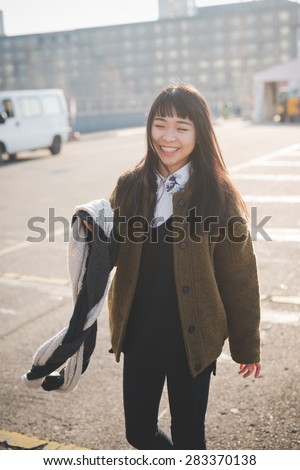 young beautiful asian hipster woman in the city - living town during sunset in backlit - smiling happy having fun with scarf