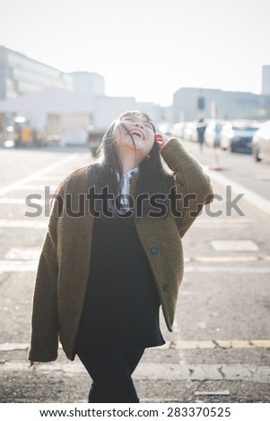 young beautiful asian hipster woman in the city - living town during sunset in backlit smiling happy having fun