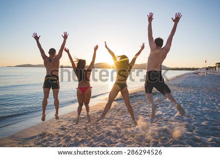 group of young multiethnic friends women and men at the beach in summertime jumping back sunset