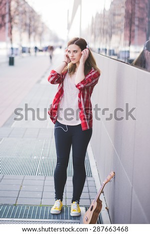 young beautiful blonde hipster woman in the city with ukulele and headphones