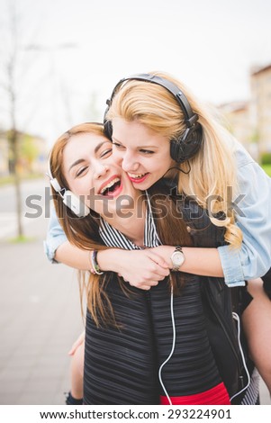 Two young blonde and brunette girls listening to music in the city having fun - music, technology, friendship concept