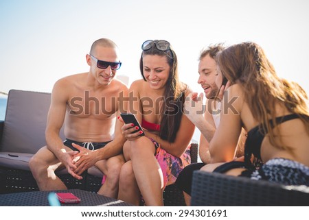 group of young multiethnic friends women and men at the beach bar in summertime using smartphone - happy hour, relax concept