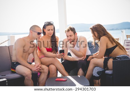 group of young multiethnic friends women and men at the beach bar in summertime using smartphone - happy hour, relax concept
