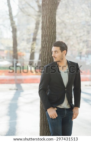 Knee-figure of a young handsome italian boy leaning on a tree in a city park posing