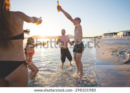 group of young multiethnic friends women and men at the beach in summertime toasting and drinking beer jumping and dancing - friendship, carefreeness concept