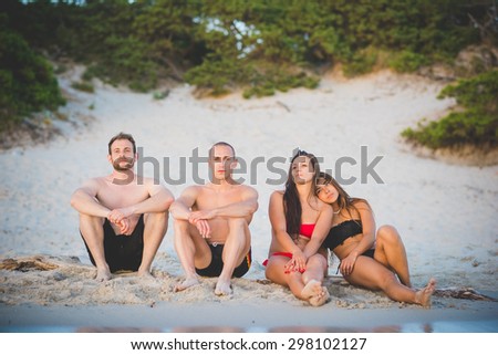 Group of young multiethnic friends seated on the foreshore in swimsuit looking at the horizon at the beach at sunset - future, relax, friendship concept