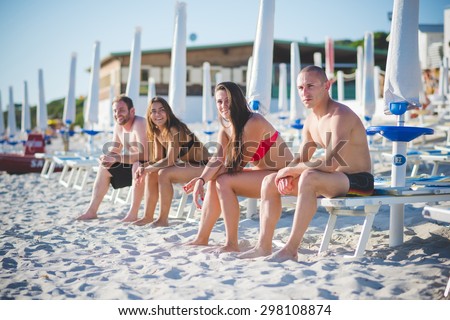 Group of young multiethnic friends seated on beach chairs in swimsuit looking at the horizon - future, relax, friendship concept