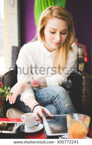 young beautiful blonde straight hair woman in the city sitting at the restaurant using tablet connected online - relax, social network, technology concepts