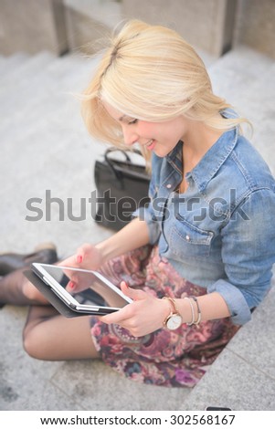 Half length of a young beautiful blonde caucasian girl seated on a staircase using a smartphone looking downward the screen - communication, technology, social network concept