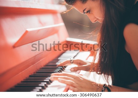 Close up of a young beautiful reddish brown hair caucasian girl playing piano - creative, performance, music concept - she is dressed with a black shirt and plays a red piano
