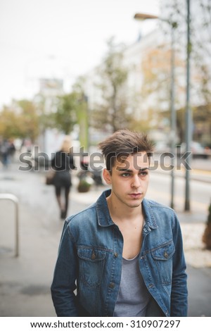 Half length of a young handsome caucasian dark model leaning on a post overlooking left with central labret and nostril piercing - rebellion, youth, diversity concept