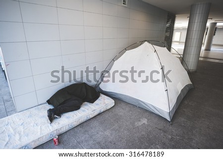 BUDAPEST - SEPTEMBER 7 : War syrian refugees at the Keleti Palyaudvar Railway Station on 1 September 2015 in Budapest, Hungary. A man sleeping on a matress covered with a jacket, beside a tent.