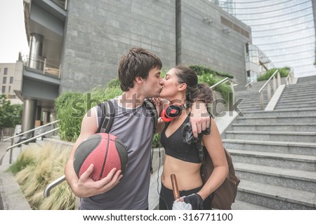 Couple of young handsome caucasian sportive man and woman walking downstairs, he is holding a basket ball in his hand and kissing his girlfriend- relaxing, break, sportive concept