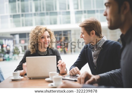 Multiracial contemporary business people working connected with technological devices like tablet and laptop, talking together, sitting in a bar - finance, business, technology concept