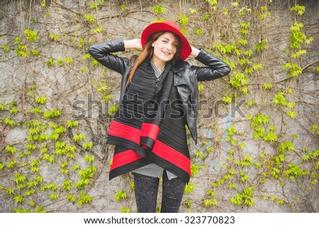 Young handsome brunette eastern fashion girl posing leaning on a wall in the city suburbs , arms behind her head, looking in camera, smiling - youth, carefreeness concept