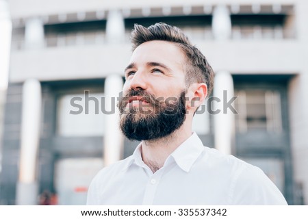Portrait of young handsome caucasian blonde modern businessman posing in the city backlight, overlooking right, smiling - successful, business concept