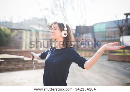 Half length of a young pretty brown hair caucasian girl listening music with headphones, holding a smartphone in her hand, overlooking right, dancing and smiling - music, relaxing, happiness concept