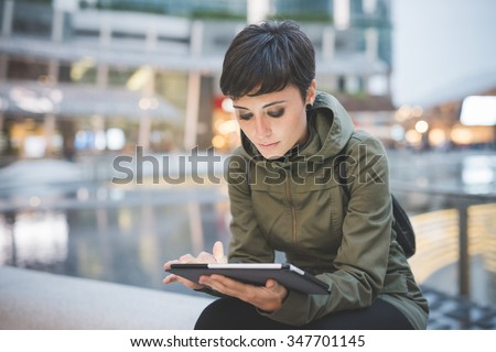 young handsome caucasian brown straight hair woman sitting in city dusk, holding tablet, looking downward screen, face illuminated by screen light - technology, social network, communication concept