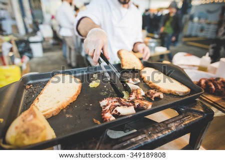 MILAN, ITALY - NOVEMBER 7: People visiting Eat Market, a street food parade with international dishes  in Milan on November, 7 2015. Close up hands chef cooking octopus on slab