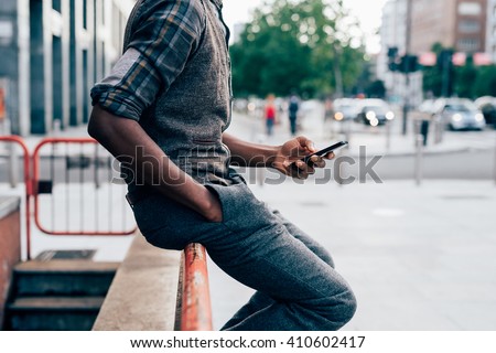 From the neck down view of young afro black man holding a smart phone, tapping the scree outdoor in the city - technology, social network, communication concept