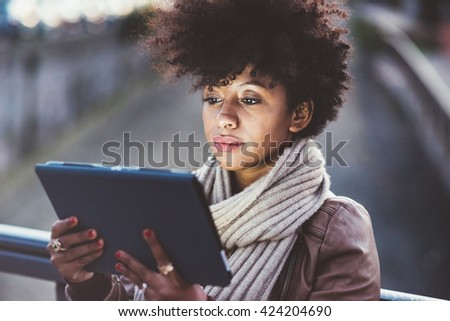 Half length of beautiful black curly hair african woman using tablet in town by night, face illuminated by screen light - technology, communication, social network concept
