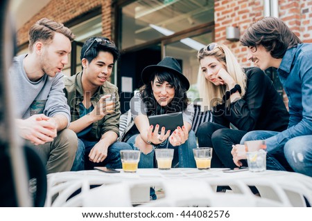 Group of young multiethnic friends sitting in a bar having a drink, talking to each other holding a smart phone, having fun - happy hour, friendship, relax concept
