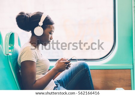 Young black woman listening music travelling by bus using smart phone hand hold, pensive - thoughtful, thinking future, music concept