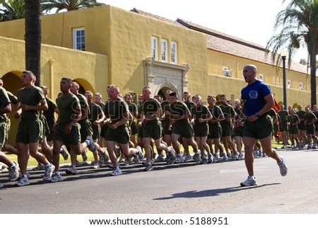 Platoon of Marine recruits running with Drill Instructor Shouting commands alongside.