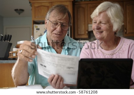 Senior romantic couple uses computer and the Internet to do some e-banking from their rural home.