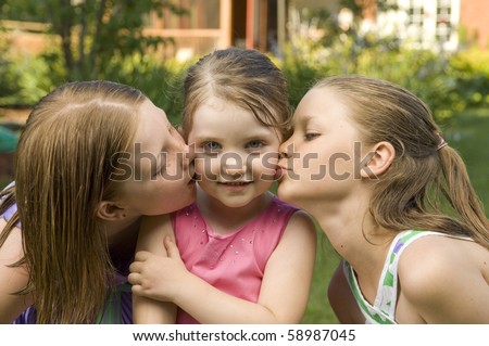 Two older sisters kiss their younger sibling.
