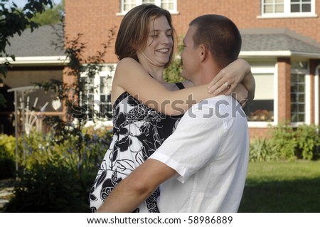 Young romantic couple plays in the backyard of their new home.