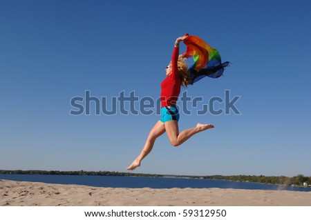 Athletic woman, wearing colourful clothes, jumps in the air with scarf in her hands.